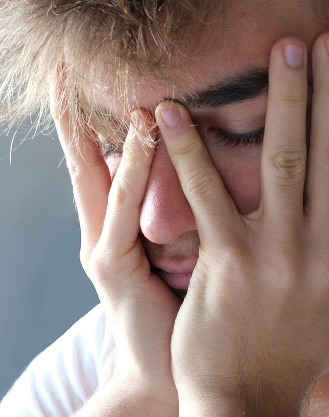 A stressed individual with face partially covered by their hands